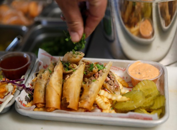 Owner and chef Alex Retodo garnishes his bacon cheeseburger lumpia dish at The Lumpia Company in Oakland, Calif., on Thursday, Feb. 8, 2024. This year will be the sixth season that the company, co-owned by local rapper E-40, have been serving their fried spring rolls to San Francisco Giants fans at Oracle Park. (Jane Tyska/Bay Area News Group)