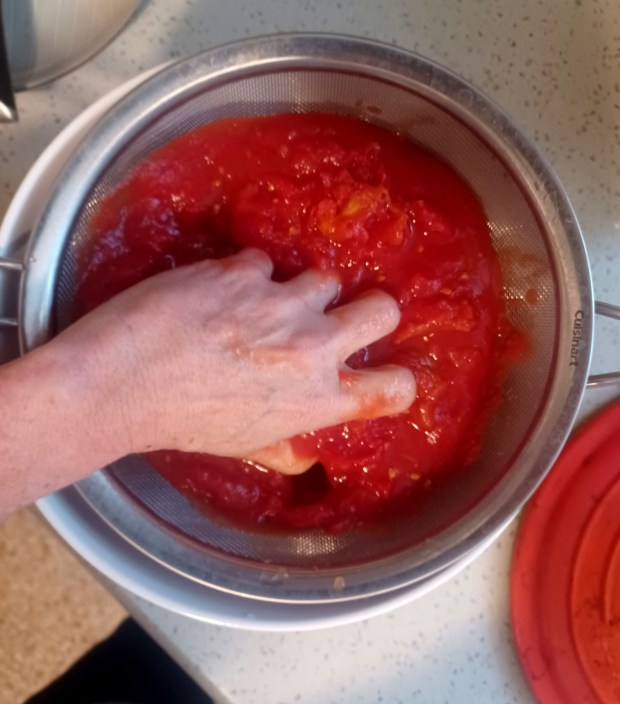 Crush the whole tomatoes by hand in a strainer, allowing the juice to drain into a bowl below. You'll use both in the recipe. (Amy Drew Thompson/Orlando Sentinel)